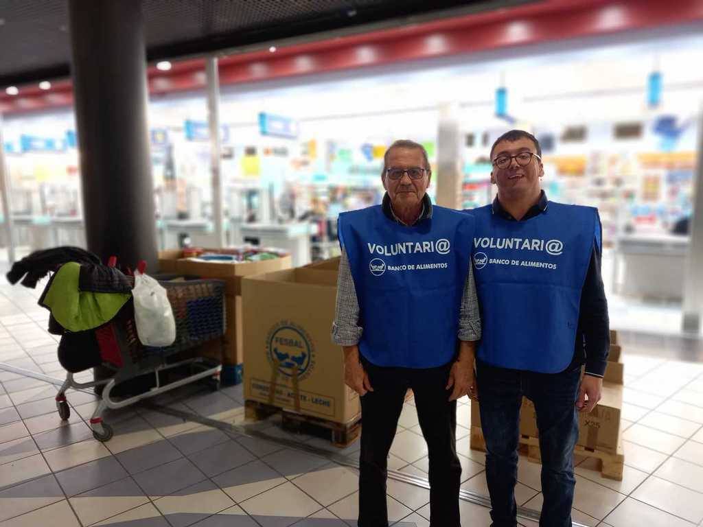 Dos voluntarios con petos junto a las cajas de recogida en un supermercado