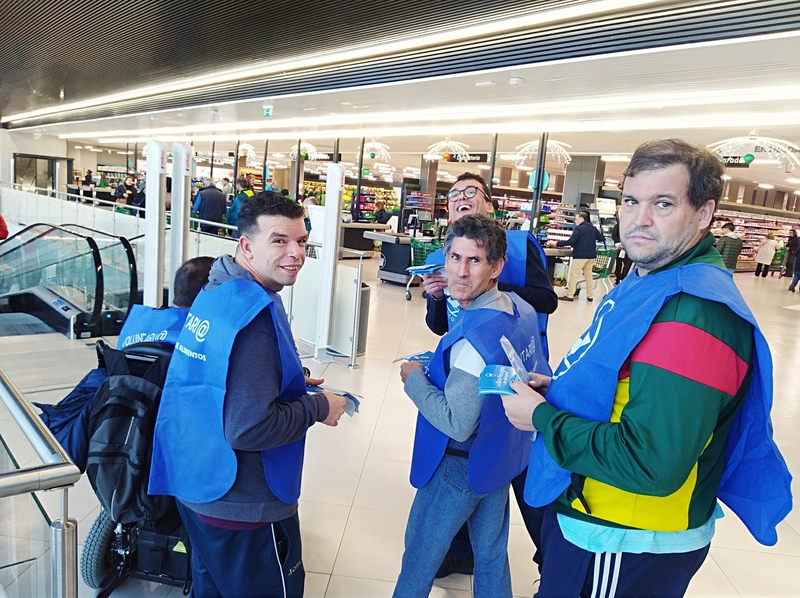 Voluntarios con petos azules repartiendo folletos en un centro comercial