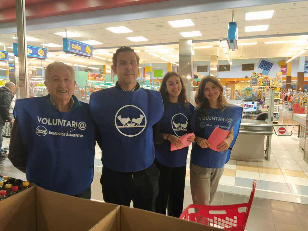 Cuatro voluntarios de varias edades junto a las cajas de recogida