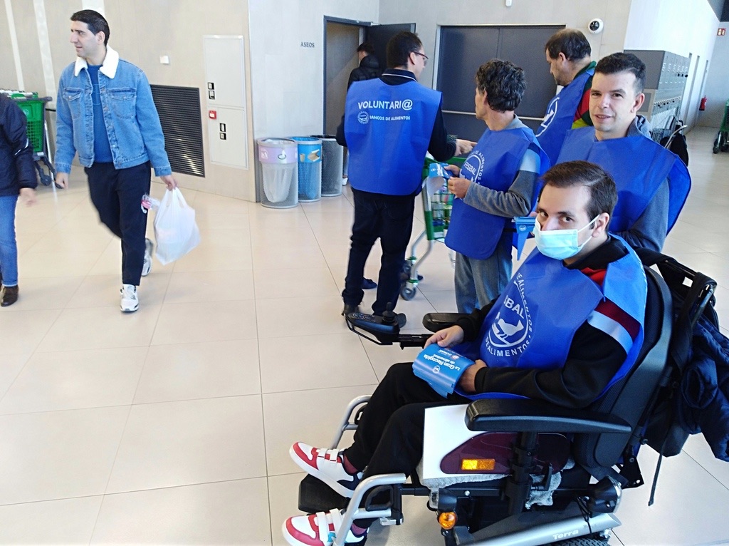 Voluntarios, uno de ellos en silla de ruedas, informando a los clientes en un centro comercial