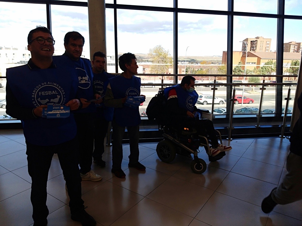 Grupo de voluntarios con folletos junto a los ventanales de un centro comercial
