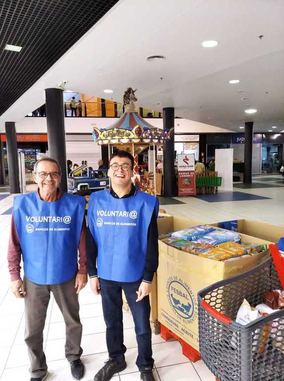 Dos voluntarios junto a un carro y cajas de alimentos