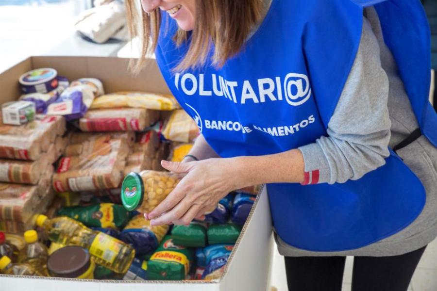 Voluntaria con peto del Banco de Alimentos clasificando alimentos en una caja